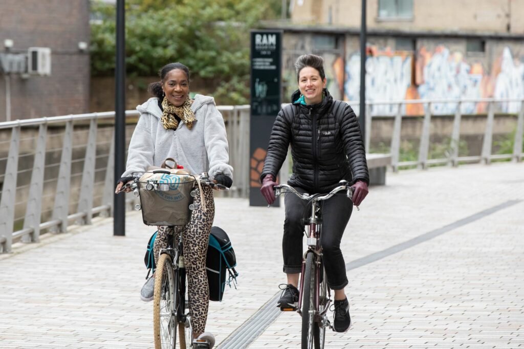 Two women cycle side by side along a quiet street